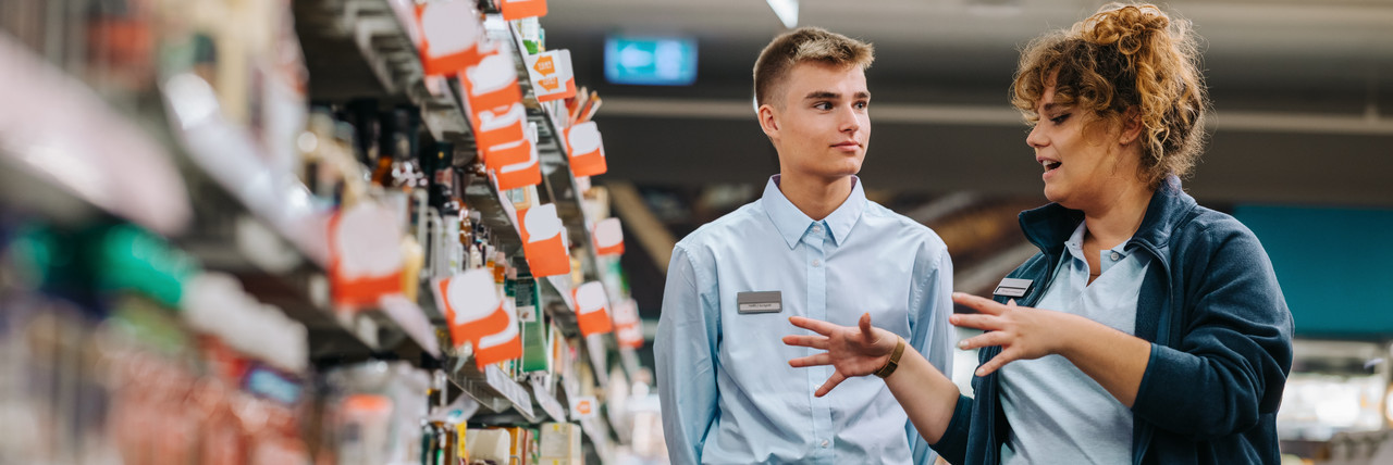 Foto: Im Supermarkt erklärt eine Ausbilderin einem Auszubildenden etwas. 