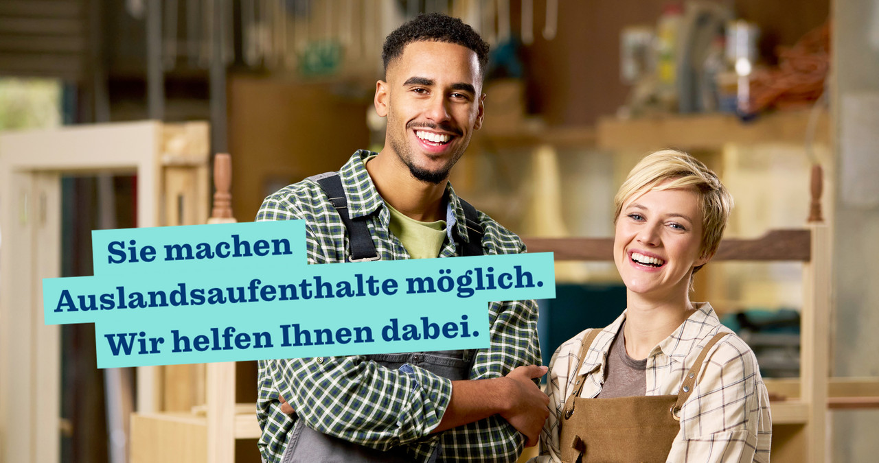 Foto: zwei Personen stehen in einer Schreinerei, die Arme verschr&auml;nkt und l&auml;cheln in die Kamera, Schriftzug: Sie machen Auslandsaufenthalte m&ouml;glich. Wir helfen Ihnen dabei.