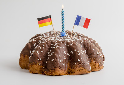 Foto eines Kuchens. Auf dem Kuchen steckt eine brennende Kerze und je eine Flagge Deutschlands und Frankreichs.