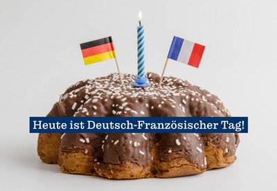 Foto eines Kuchens. Auf dem Kuchen steckt eine brennende Kerze und je eine Flagge Deutschlands und Frankreichs. &Uuml;ber den Kuchen l&auml;uft der Schriftzug "Heute ist Deutsch-Franz&ouml;sischer Tag!".