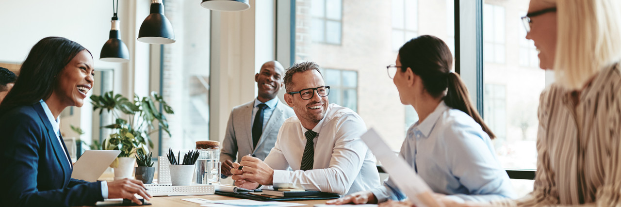 Foto: 5 diverse Personen lachend bei einem Businessmeeting.