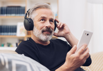Foto: Mann mittleren Alters hört Musik oder Podcast über Kopfhörer.