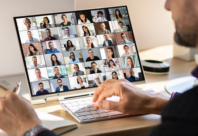 Foto: ein Mann sitzt vor dem Notebook. auf dem Bildschirm ist eine Videokonferenz mit vielen Videokacheln zu sehen. 