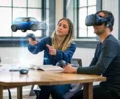 Foto: zwei Arbeitskollegen (eine Frau und ein Mann) prüfen ein Automobil-Designkonzept. Der Mann trägt eine VR-BRille, die Frau steuert. Das virtuelle Auto wird vor ihr in der Luft dargestellt.
