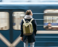 Foto: ein junger Mann mit Rucksack auf dem Rücken vor einem einfahrenden Zug.