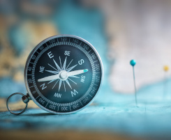 Foto: Kompass auf einer Weltkarte, in welcher Pinnadeln stecken.