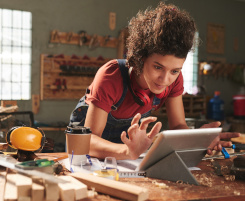 Foto: Auszubildende sucht auf einem Tablet in einer Holzwerkstatt.