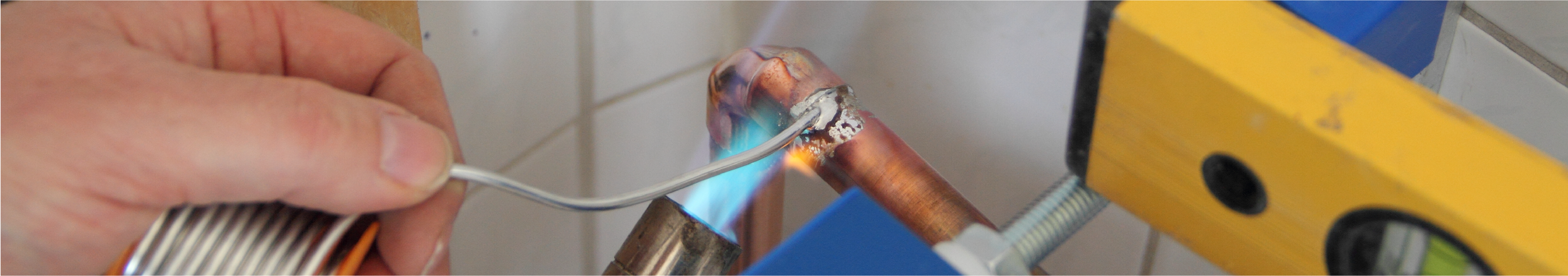Foto: Das Bild zeigt wie ein Kupferrohr in einem gefliesten Badezimmer gelötet wird.
